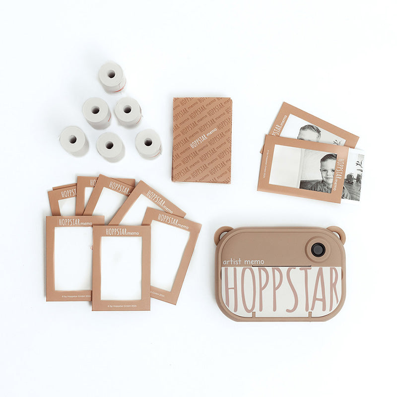 Set-Inhalt der Hoppstar Artist Memo Kamera: Kamera, mehrere Fotopapierrollen, bedruckte Kartenrahmen und eine braune Verpackung.