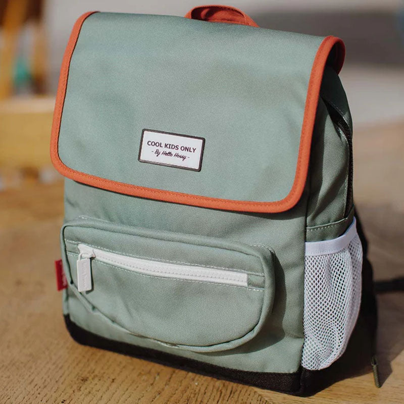 Rucksack steht auf einem Holztisch, grünes Design mit roten Akzenten und weißem Reißverschluss.