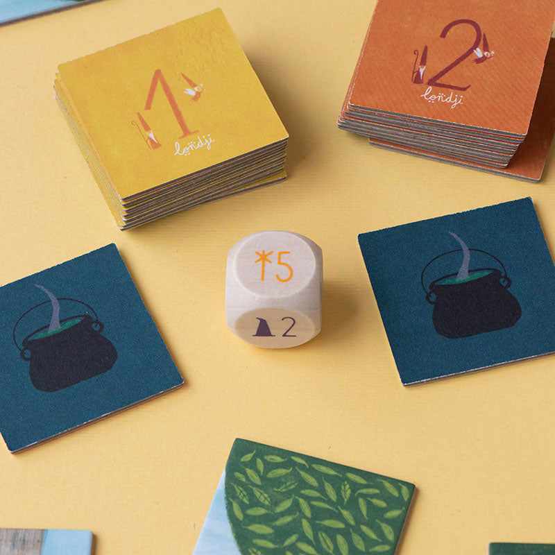 Würfel und quadratische Spielkarten mit Kesselsymbolen und Zahlen.