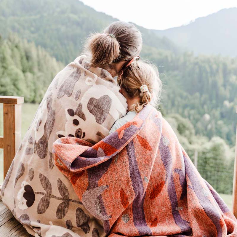 Mutter und Tocher kuscheln mit zwei Kuscheldecken und genießen die Aussicht auf den Berg