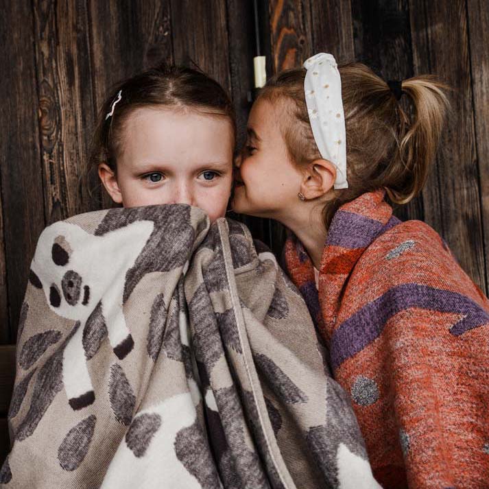 Zwei Kinder sitzen nebeneinander und Kuscheln mit Kuscheldecken