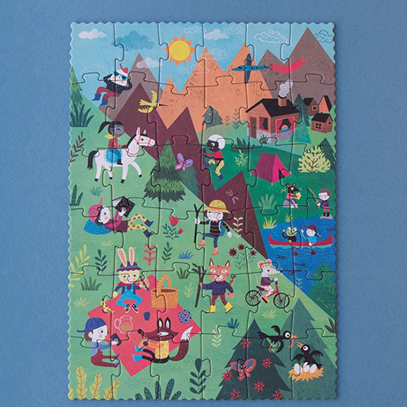 Ein buntes Puzzle mit einer sommerlichen Bergszene: Kinder und Tiere beim Wandern, Picknick, Radfahren und Kanufahren inmitten grüner Wiesen und Berge.