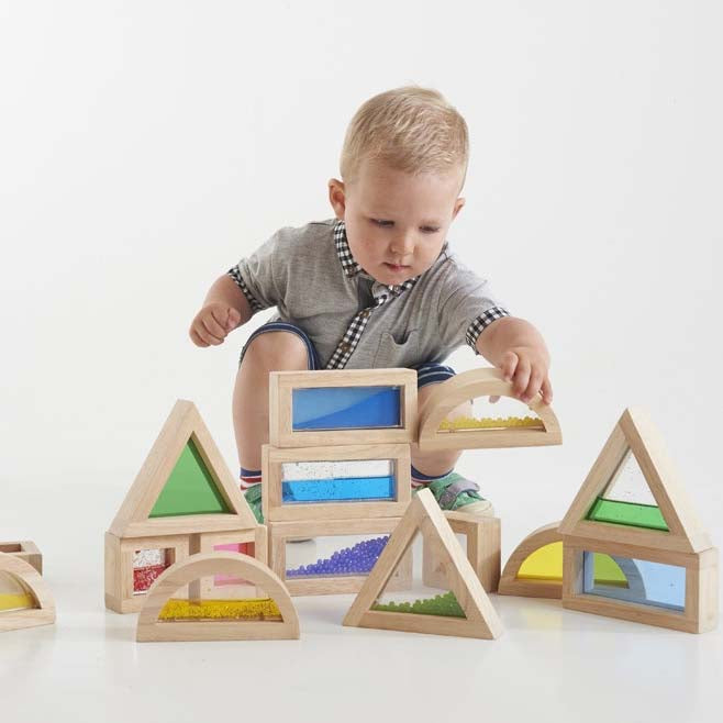 kleiner Bub sitzt hinter sensorischen bausteinen und hebt einen gelb gefüllten Baustein auf