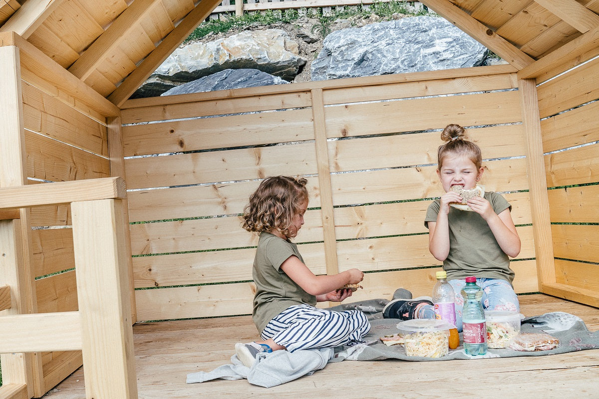 zwei Kinder sitzen im Picknickhäuschen und naschen ihr Picknick