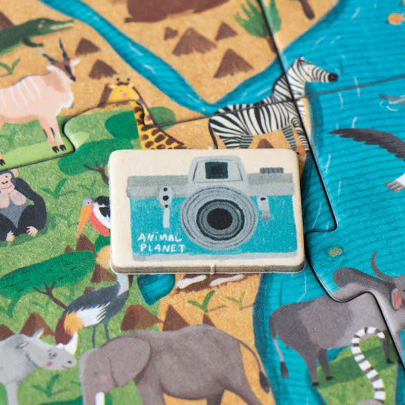 Holzplättchen in Form einer Kamera liegt auf dem Puzzle zwischen Elefanten, Zebras und Giraffen.