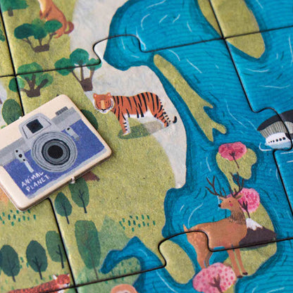 Kamera-Spielstein auf Puzzle-Ausschnitt, mit Tiger, Reh und Flusslandschaft im Hintergrund.