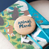 Nahaufnahme des Holzknopfs mit Aufschrift „Animal Planet“, auf dem bunt illustrierten Verpackungsdeckel.