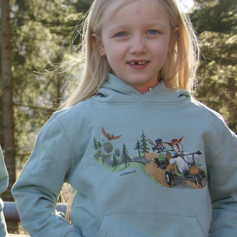 Kind zeigt Vorderseite eines aloegrünen Bio-Baumwollhoodies, zeigt weiches Material, natürliche Farbe und liebevolle Verarbeitung