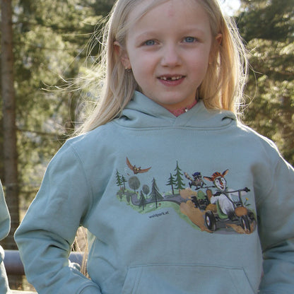 Kind zeigt Vorderseite eines aloegrünen Bio-Baumwollhoodies, zeigt weiches Material, natürliche Farbe und liebevolle Verarbeitung