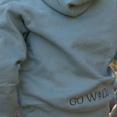 Rückansicht eines aloegrünen Bio-Baumwollhoodies, weicher Stoff und sorgfältige Nähte, getragen von einem Kind im Freien