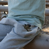 Nahaufnahme der grauen Bio-Baumwollhose mit Waschbären-Print, zeigt weichen Stoff und sorgfältige Verarbeitung, getragen von einem Kind im Grünen