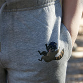 Kind hat Hände in der Tasche der grauen Bio-Baumwollhose mit Waschbär im Sturzhelm, nachhaltige Outdoor-Kleidung für Kinder im Wald.