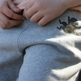 Kinderhose aus grauer Bio-Baumwolle mit Waschbären-Motiv, ideal für Bewegung und Spiel im Freien, natürliche Qualität und hoher Tragekomfort