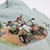 Nahaufnahme des T-Shirt-Motivs auf grüner Vorderseite: Ziege und Waschbär flitzen gemeinsam im Go-Kart, farbenfroh und kindgerecht.