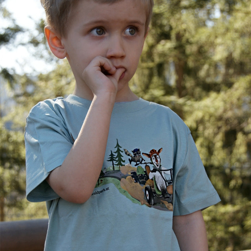 Kind im Wald mit grünem Go Wild Shirt, detailreiche Vorderseite sichtbar, zeigt Spaß an Bewegung und Abenteuer in der Natur