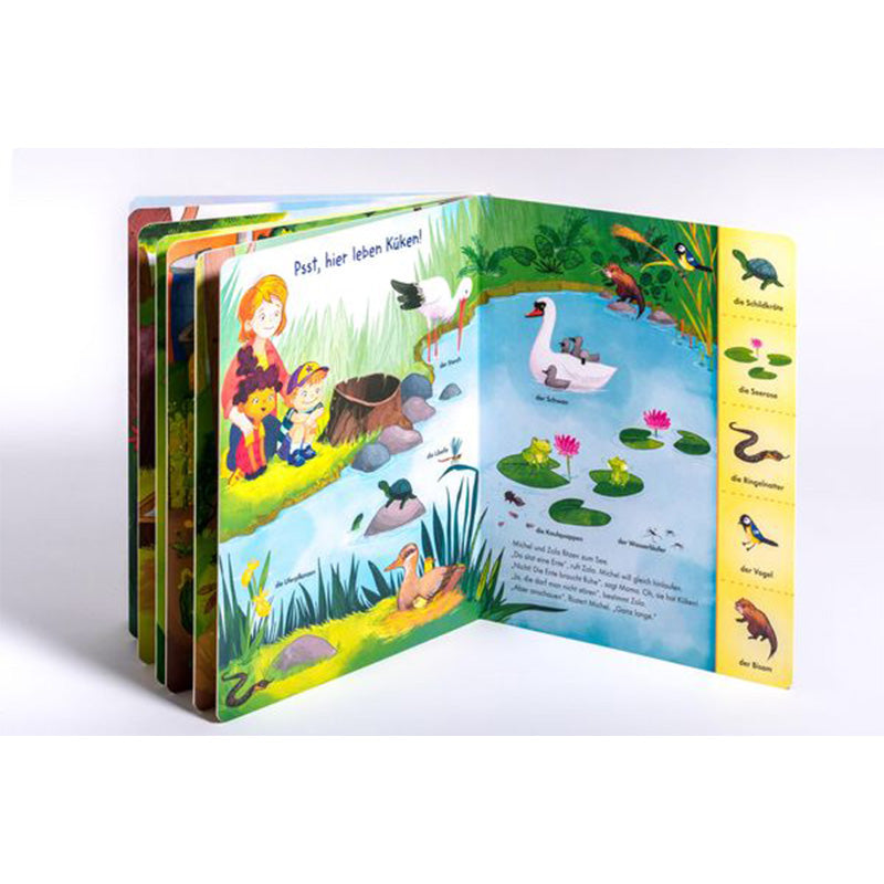 Buchseite mit Teichszene. Kinder beobachten Tiere wie Schwan, Storch und Frösche an einem See. Rechts Vokabel-Leiste mit Tieren.