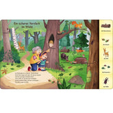 Buchseite „Ein sicheres Versteck im Wald“. Kind und Oma entdecken Tiere im Wald wie Eule, Specht und Fuchs. Begriffe am Seitenrand.