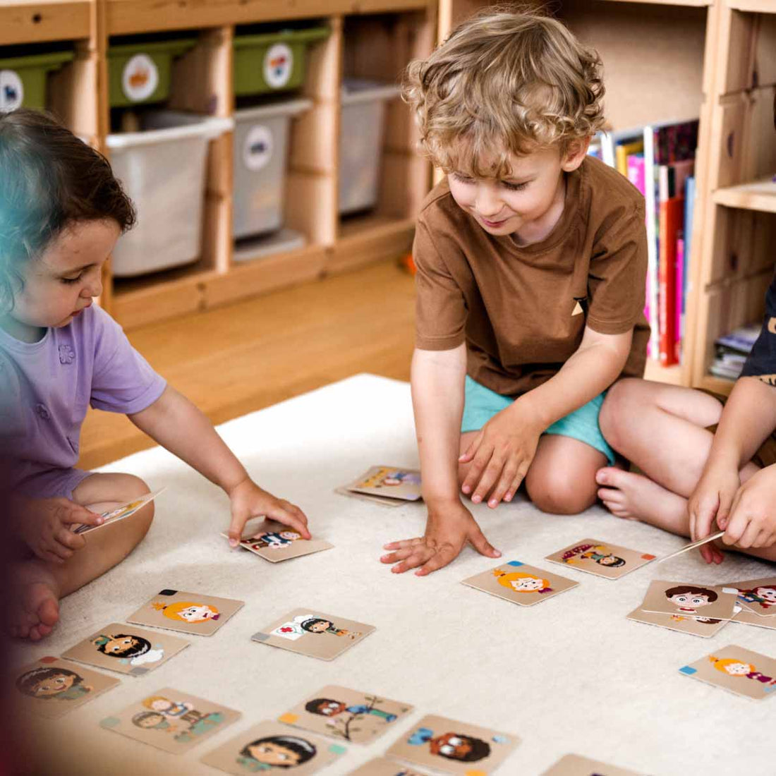 drei Kinder spielen am Teppich mit den Emotions Memokarten