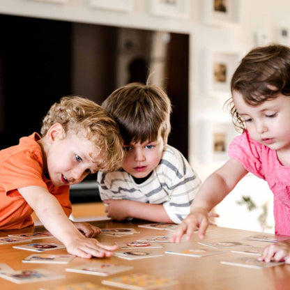 drei Kleinkinder sitzen am tisch und spielen das Emotionen Memospiel