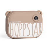Beige Kinderkamera „Hoppstar Artist Memo“ mit rundem Objektiv und niedlichen Ohren an der Oberseite.