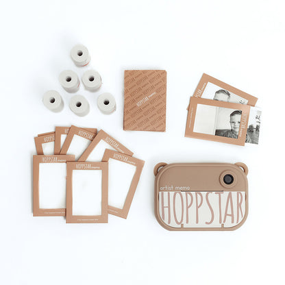Set-Inhalt der Hoppstar Artist Memo Kamera: Kamera, mehrere Fotopapierrollen, bedruckte Kartenrahmen und eine braune Verpackung.