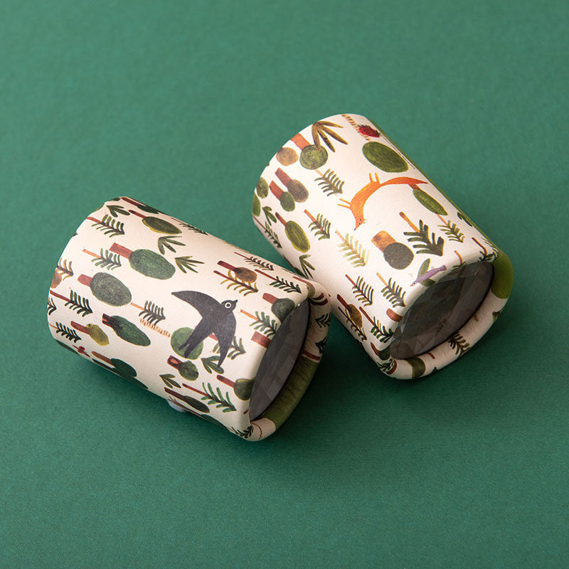 Zwei Kaleidoskope mit Waldmotiven, auf grünem Hintergrund liegend.