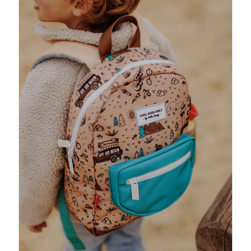 Kind trägt den beigen Rucksack mit grünem Fach und Waldmotiv im Freien auf dem Rücken.