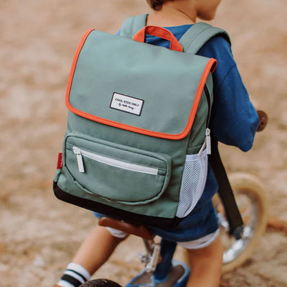 Kind trägt den grünen Rucksack mit rotem Rand und weißen Details im Freien.
