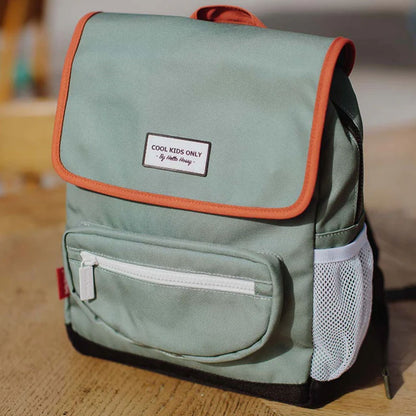 Rucksack steht auf einem Holztisch, grünes Design mit roten Akzenten und weißem Reißverschluss.