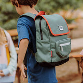 Kind trägt den grünen Rucksack mit rotem Rand und weißen Details im Freien.