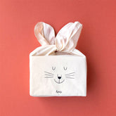 Zusammengefaltete Stofftasche in Form eines Hasengesichts mit zu Ohren gebundenen Griffen.