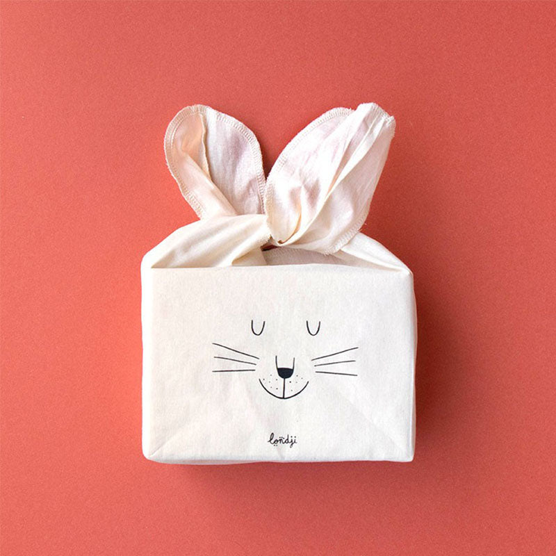 Zusammengefaltete Stofftasche in Form eines Hasengesichts mit zu Ohren gebundenen Griffen.