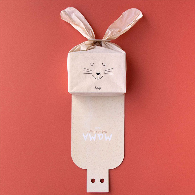 Verpackung halb geöffnet, Stofftasche mit Hasengesicht und Hasenohren darauf platziert.