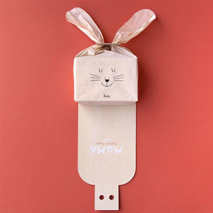 Verpackung halb geöffnet, Stofftasche mit Hasengesicht und Hasenohren darauf platziert.