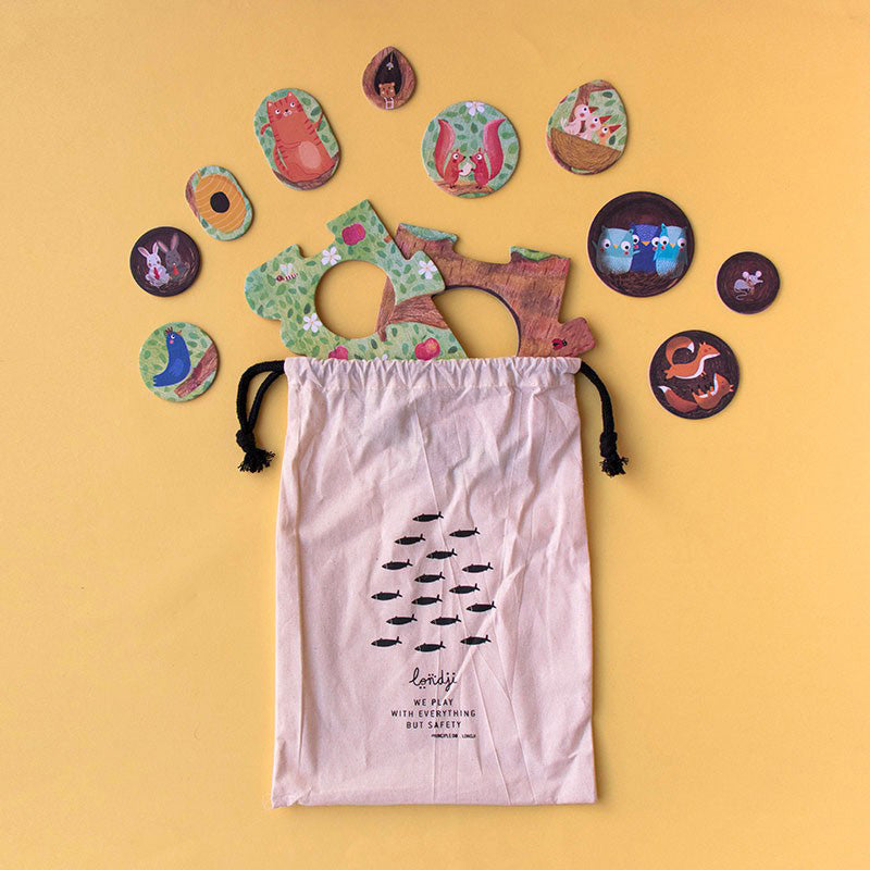 Stoffbeutel mit schwarzem Fischmuster, daneben verstreut bunte runde Puzzleteile (Tiere und Baumteile).