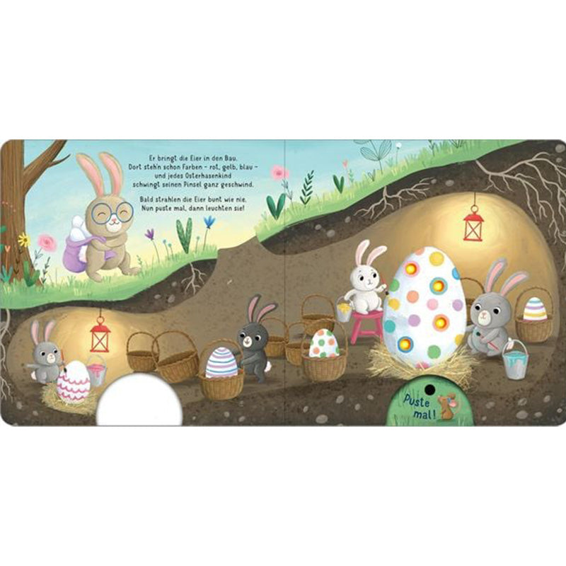 Buchseite: Unterirdischer Hasenbau mit mehreren Osterhasen, die bunte Eier bemalen und Körbe füllen; das große Ei leuchtet, wenn man pustet.