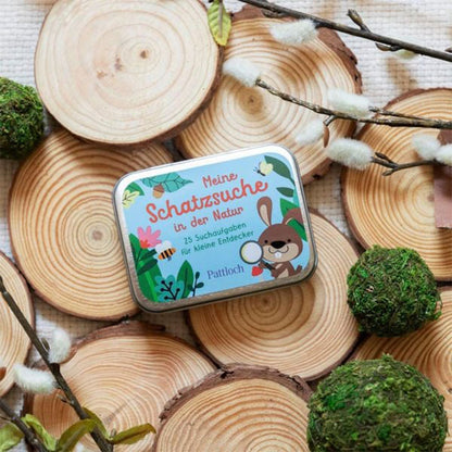 Die Schatzsuche-Box liegt dekorativ auf Holzscheiben und Moos, umgeben von Zweigen – Naturkulisse.