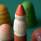 Nahaufnahme einer bemalten Holzfigur in Form eines Zwergs mit roter Mütze und weißem Körper, im Hintergrund unscharf weitere Spielfiguren wie Baum und Pilz.