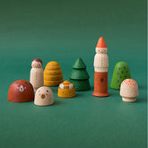 Mehrere bemalte Holzfiguren aus dem Set „My Wooden World – Forest“ auf grünem Hintergrund, darunter Bär, Kind, Pilze, Bäume, Bienenstock und Zwerg.