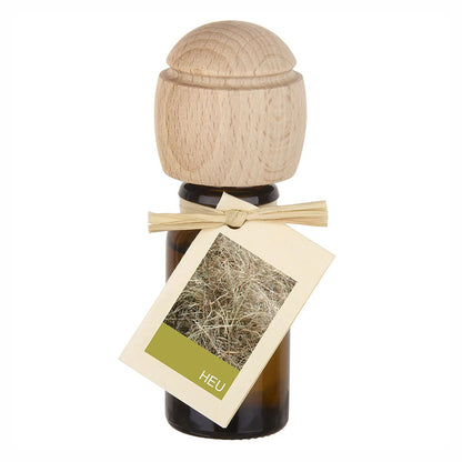 Raumduftflasche mit Holzaufsatz und Etikett Heu, zeigt getrocknetes Heu in Nahaufnahme.