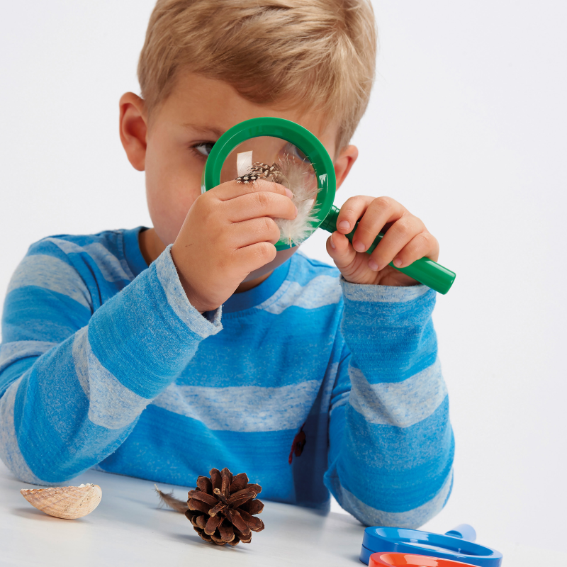 Kind spielt mit Regenbogenlupe in Grün