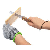 Person sägt ein Holzbrett mit einer Handsäge, während sie schnittfeste Handschuhe trägt.