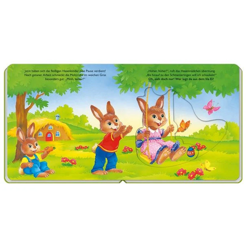 Buchseite: Drei Hasenkinder spielen auf einer grünen Wiese vor einem kleinen Strohhäuschen, eines schaukelt, die anderen sehen zu und essen Möhren.