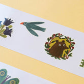 Nahaufnahme eines Tattoos mit einem blauen Vogel und einem Bären im Blätterrahmen.