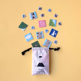 Stoffbeutel von Londji mit Spielplättchen, die herausfliegen, auf gelbem Hintergrund arrangiert.