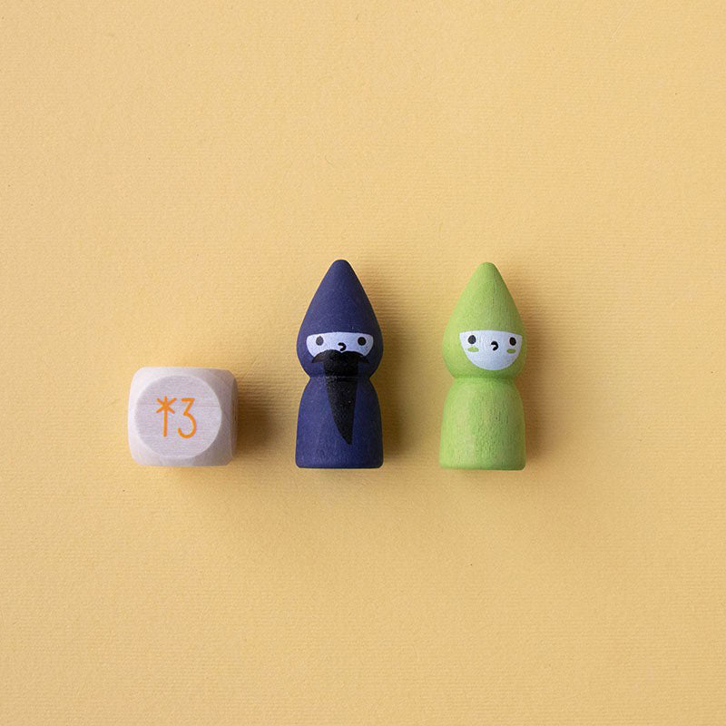 Zwei Spielfiguren – Zauberer (blau) und Fee (grün) – neben einem Holzwürfel mit oranger Stern-Zahl auf gelbem Hintergrund.