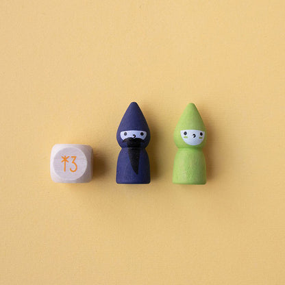 Zwei Spielfiguren – Zauberer (blau) und Fee (grün) – neben einem Holzwürfel mit oranger Stern-Zahl auf gelbem Hintergrund.