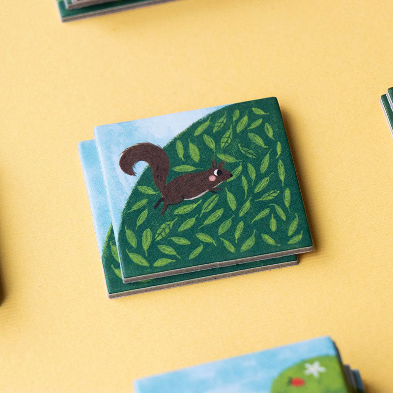 Quadratische Karte mit einem gezeichneten Eichhörnchen auf grünem Blätterhintergrund.
