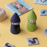 Zwei Spielfiguren aus Holz – ein Zauberer in Dunkelblau und eine Fee in Grün – auf gelbem Hintergrund.