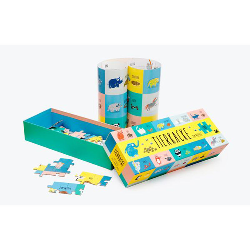 Puzzlebox mit zusammengerolltem, fertigem Puzzle, zeigt bunte Tierfelder und Kacke-Illustrationen.